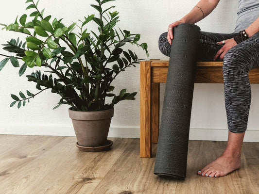 woman sitting down with her yoga mat, plant in background 